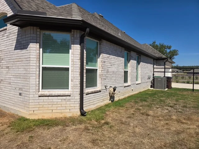 Black seamless gutters and downspout installed on a white brick home