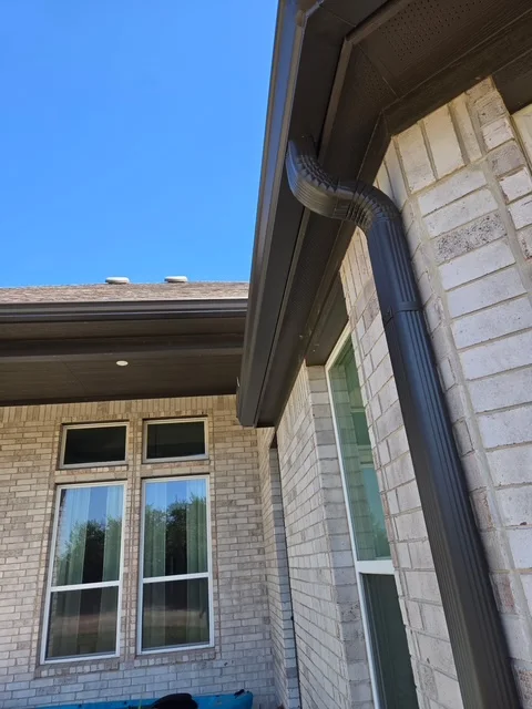 Close view of a dark downspout routed beneath a covered patio