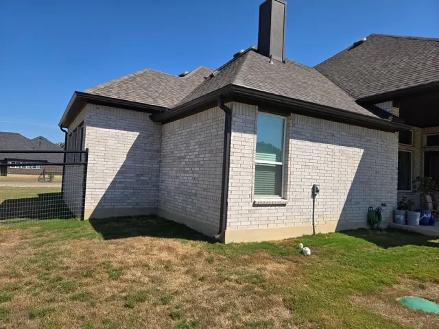 Black seamless gutters wrapping the roofline of a white brick home