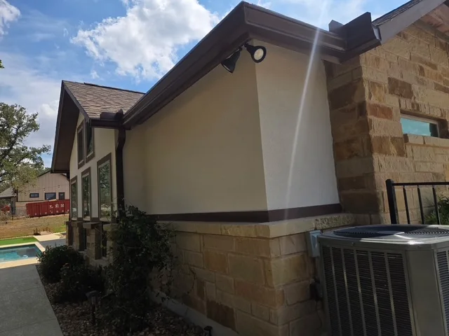 Dark gutter run fitted around a stucco and stone exterior